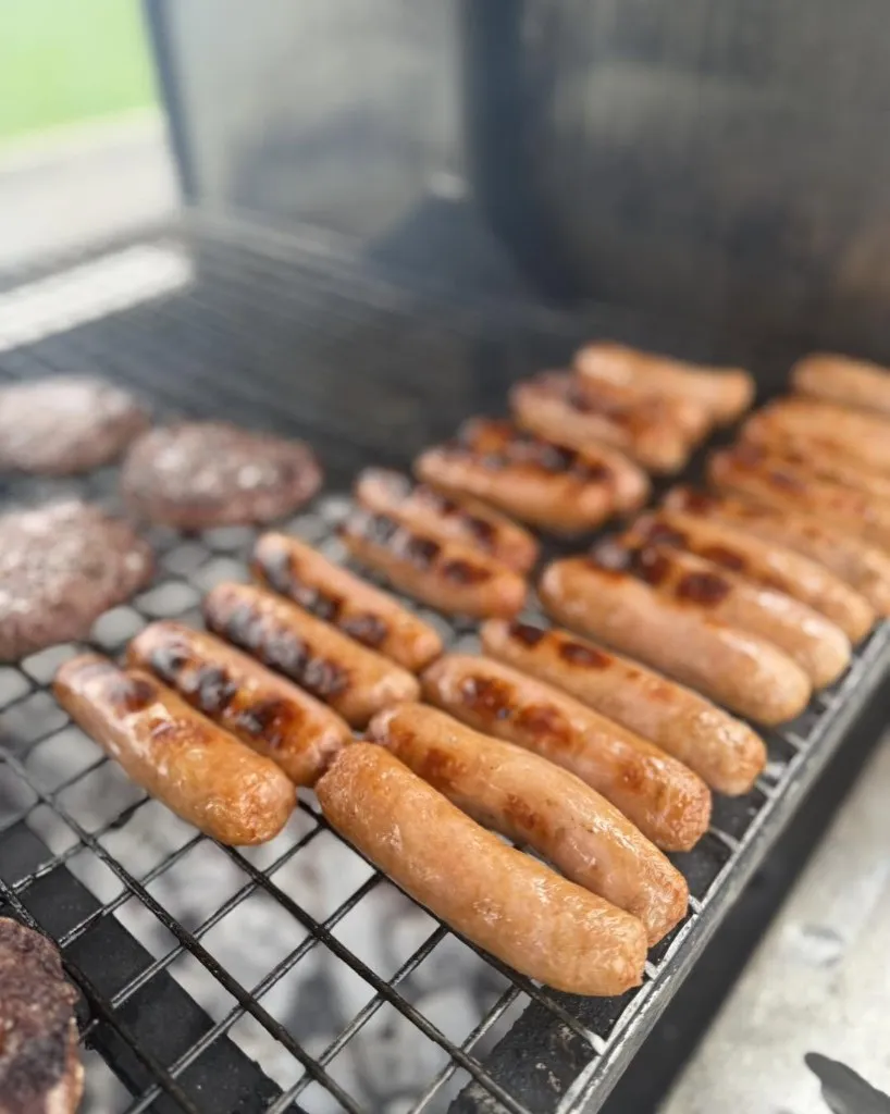 Rows of sausages and beef burgers on the grill rack