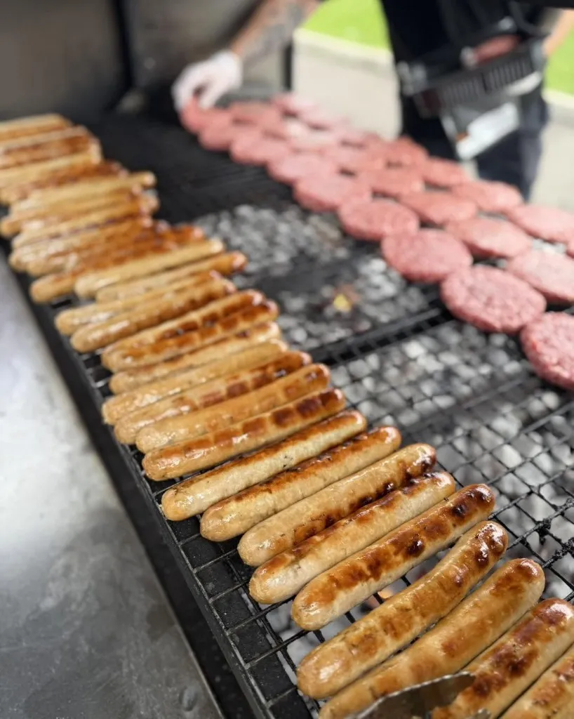Sausages and burger patties sizzling on the BBQ grill